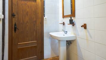 A wooden door with a handle, a white sink with a mirror above it, and a tiled wall.