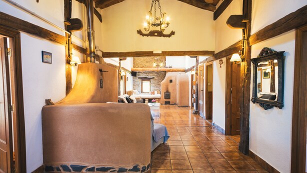 A corridor with a covered seating area, stone walls, wooden beams, and a chandelier.