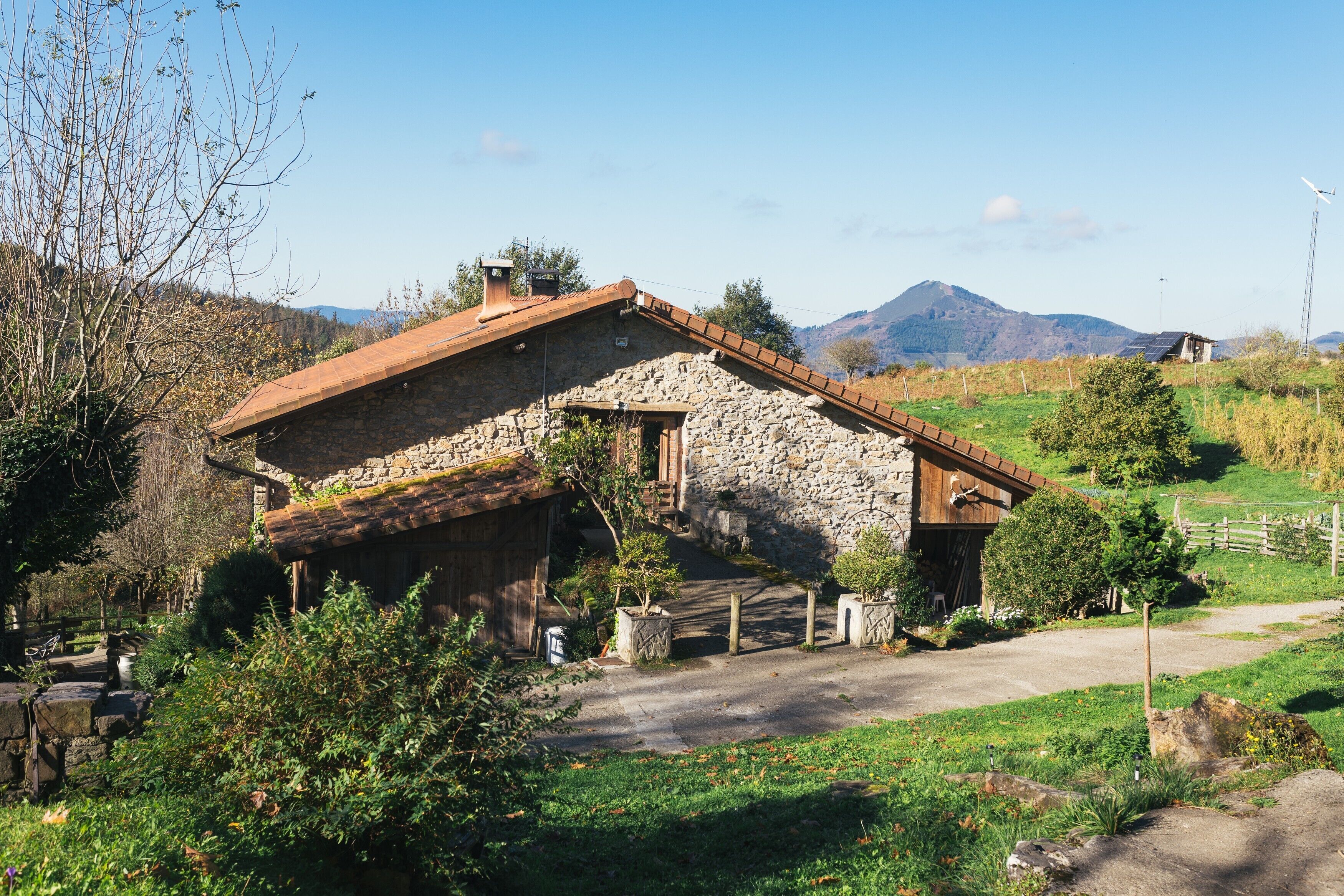 Un edificio in pietra rustica con tetto spiovente, immerso nel verde sotto un cielo sereno.