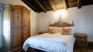 A bedroom with a wooden wardrobe, a bed with white bedding, a wooden headboard, and a nightstand with a lamp.