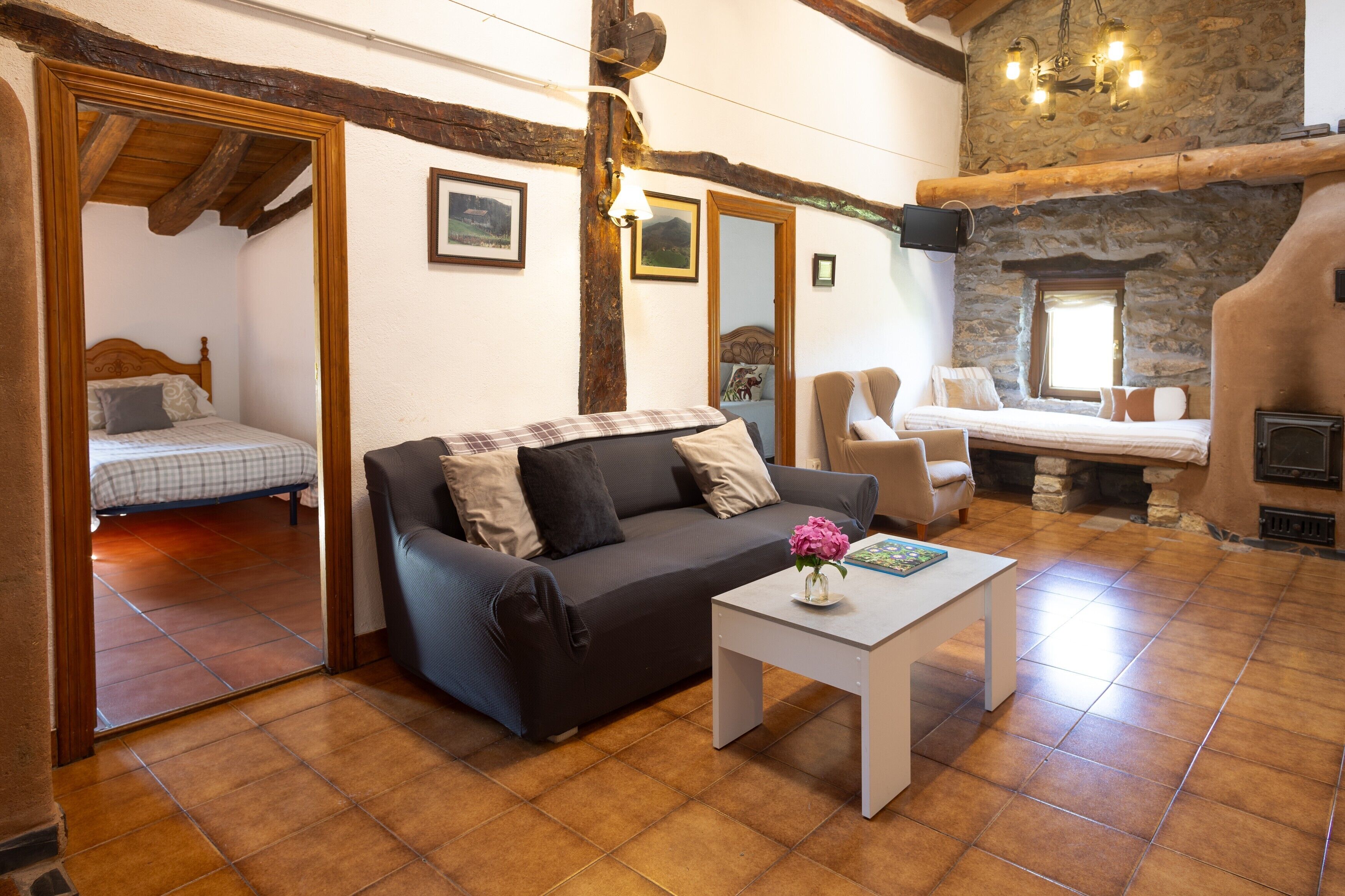 A cozy room with a sofa, a small table with a vase, a fireplace, and a bed in the corner.