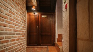 A hallway with a brick wall, wooden double doors, a small table, and a staircase. - Country House 'El Desvan Del Brigante' with Balcony, Wi-Fi and Air Conditioning (Lerma)