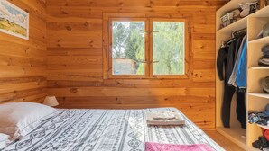 A wooden cabin room with a bed, a window, a wardrobe, and a shelf with items. - Holiday Home 'Le Colibri' with Private Pool, Wi-Fi and Air Conditioning (La Ciotat)