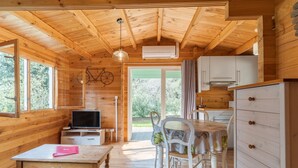 A wooden cabin interior with a dining table, chairs, a television, and a kitchen area. - Holiday Home 'Le Colibri' with Private Pool, Wi-Fi and Air Conditioning (La Ciotat)