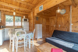 Ein Holzblockhaus-Innenraum mit Esstisch, Stühlen, einer Couch, einer Küchenzeile und einer Uhr an der Wand.