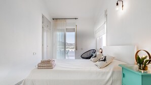 Ein Schlafzimmer mit Bett, Nachttisch, Sessel und Blick ins Freie.