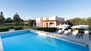 A swimming pool with lounge chairs and umbrellas, a building with a white facade and red roof, and greenery in the background. - Villa 'Leale Plemmirio' with Private Pool, Wi-Fi and Air Conditioning (Siracusa)
