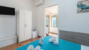 A bedroom with a bed, a wardrobe, a TV, and a bathroom visible through an open door. - Villa 'Leale Plemmirio' with Private Pool, Wi-Fi and Air Conditioning (Siracusa)