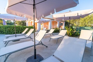 Des fauteuils de jardin avec parasols, une terrasse carrelée et un bâtiment en arrière-plan.