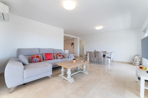 A modern living room with a grey sofa, a wooden coffee table, and a dining area with a white table and chairs. - Apartment 'Paraiso' with Sea View, Wi-Fi and Air Conditioning (Fuengirola)