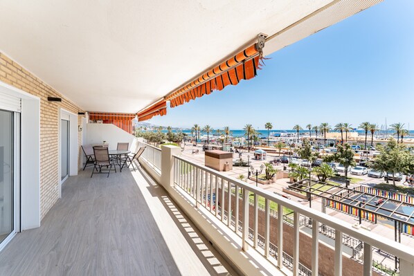 A balcony with a view of a marina, outdoor seating, and a clear sky.