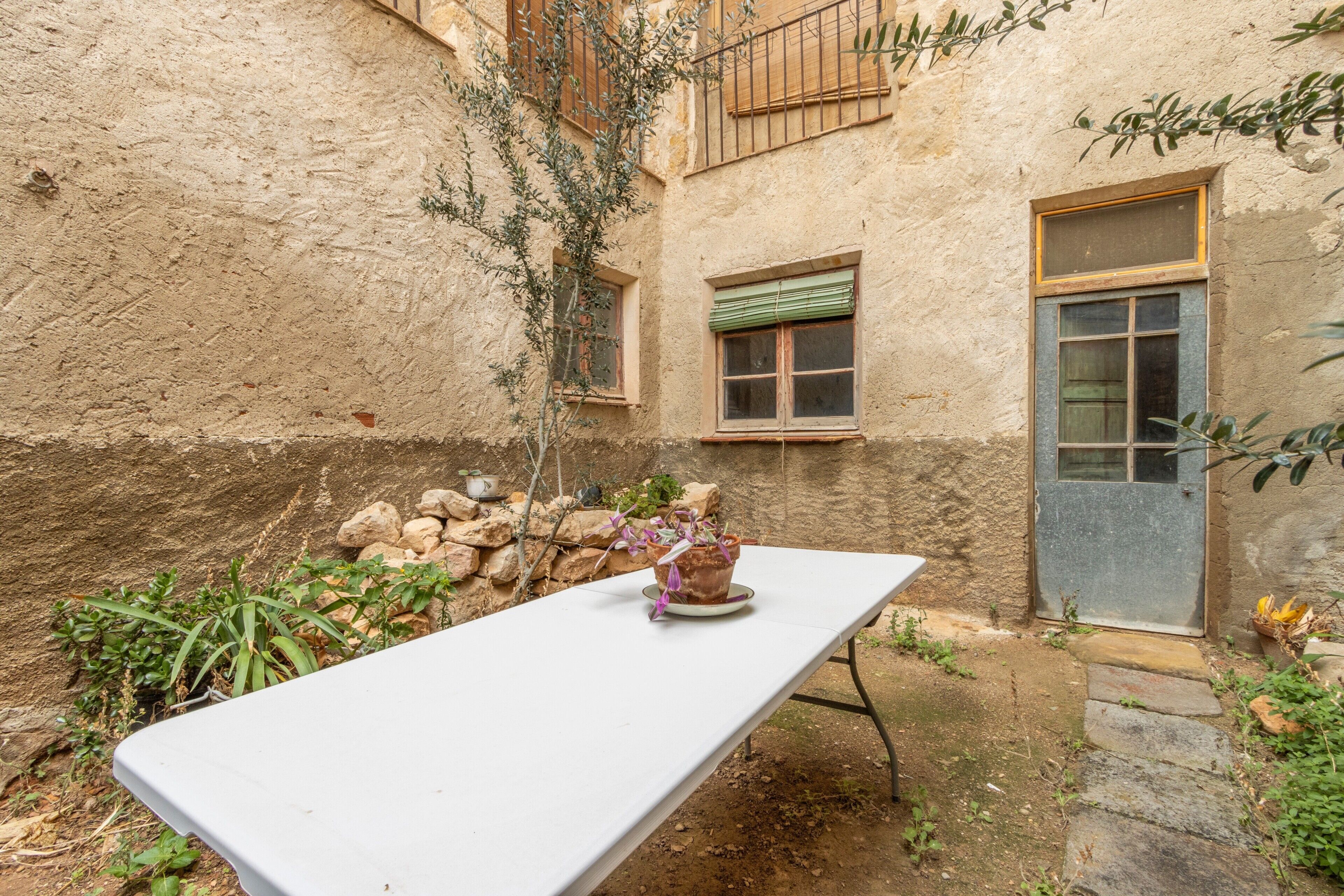 Una mesa blanca en un patio exterior con una planta en maceta, un muro de piedra y una puerta.