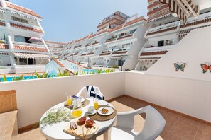 Une terrasse sur le toit, avec une table dressée pour le petit-déjeuner, d’où l’on peut admirer une piscine et les bâtiments avoisinants.