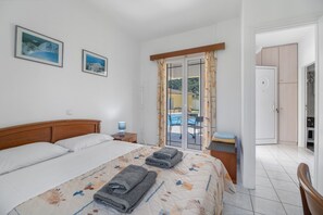 A bedroom with a bed, a nightstand, a desk, a chair, a balcony with a table and chairs, and a wardrobe.