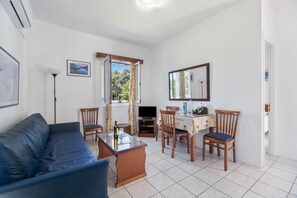 A living room with a sofa, dining table, chairs, a TV, and a window with a view.