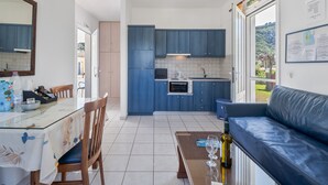A modern kitchen with blue cabinets, a dining area with a glass table, and a blue sofa. - Holiday Home 'Dioni' with Mountain View, Wi-Fi and Air Conditioning (Lefkada)
