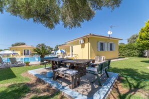 A yellow villa with a swimming pool, outdoor seating, and a satellite dish.