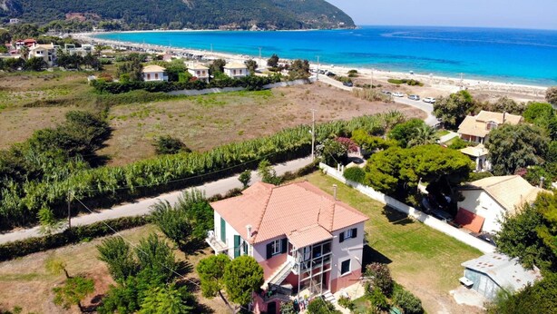 A coastal residential area with houses, a beach, and a hilly backdrop.