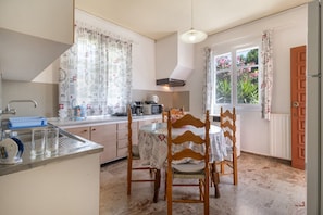 Una cucina con tavolo, sedie, lavello e una finestra con tende.