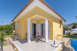 Een geel gebouw met een overdekte patio, witte kolommen en een betegelde vloer.