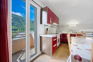 A kitchen with red cabinets, a wooden table, and a view of a forest through a sliding door.