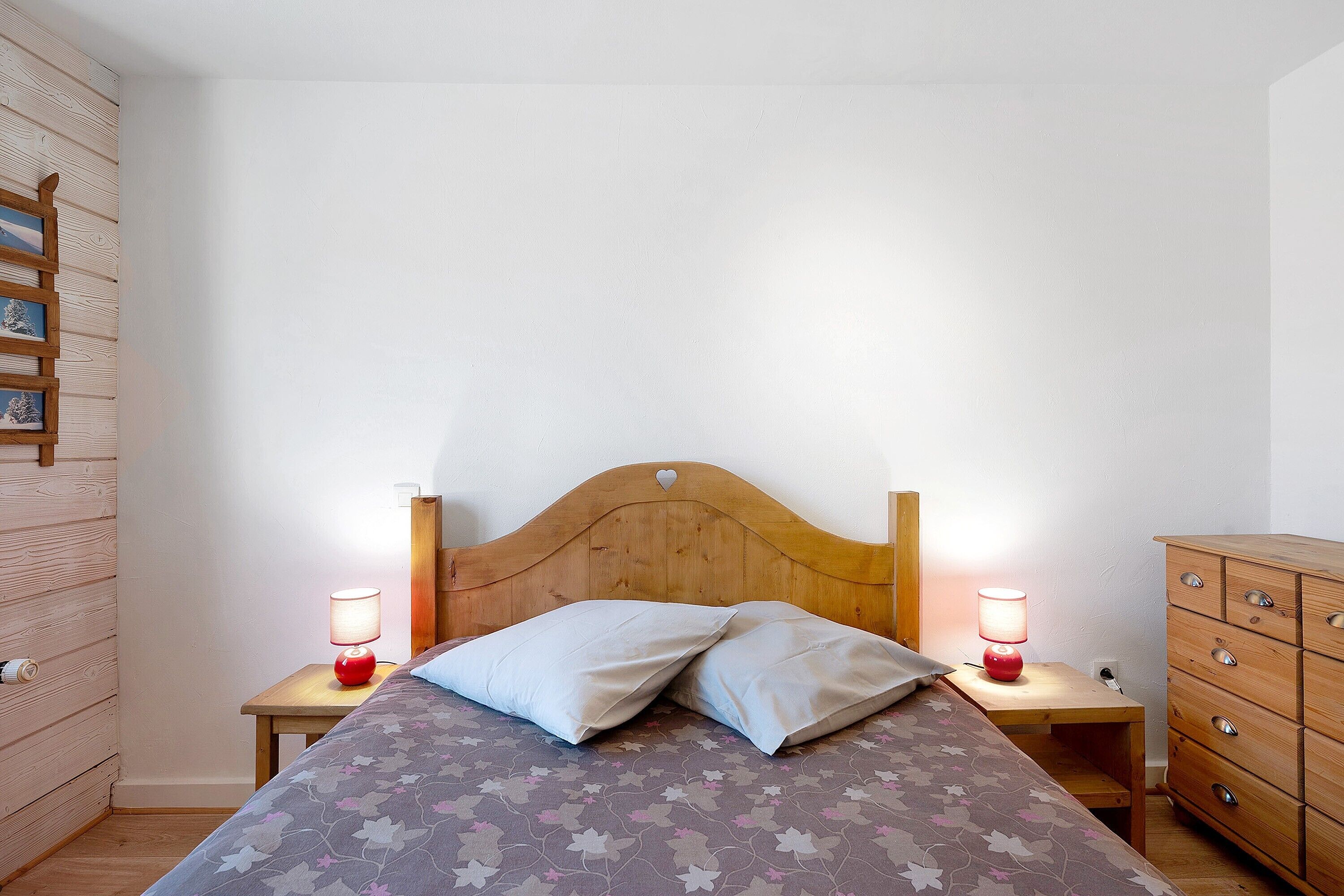 Een slaapkamer met een houten hoofdbord, twee nachtkastjes met lampen, een bed met bloemenbeddels en een houten dressoir.