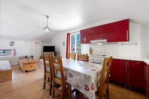 Un comedor con mesa y sillas, una cocina con armarios rojos y una ventana con vistas a zonas verdes.