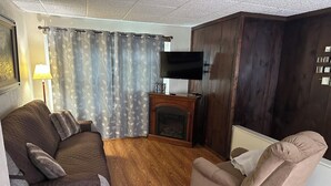 Ein Wohnzimmer mit einer Couch, einem Sessel, Holzboden, Kamin und einem Flachbildfernseher.