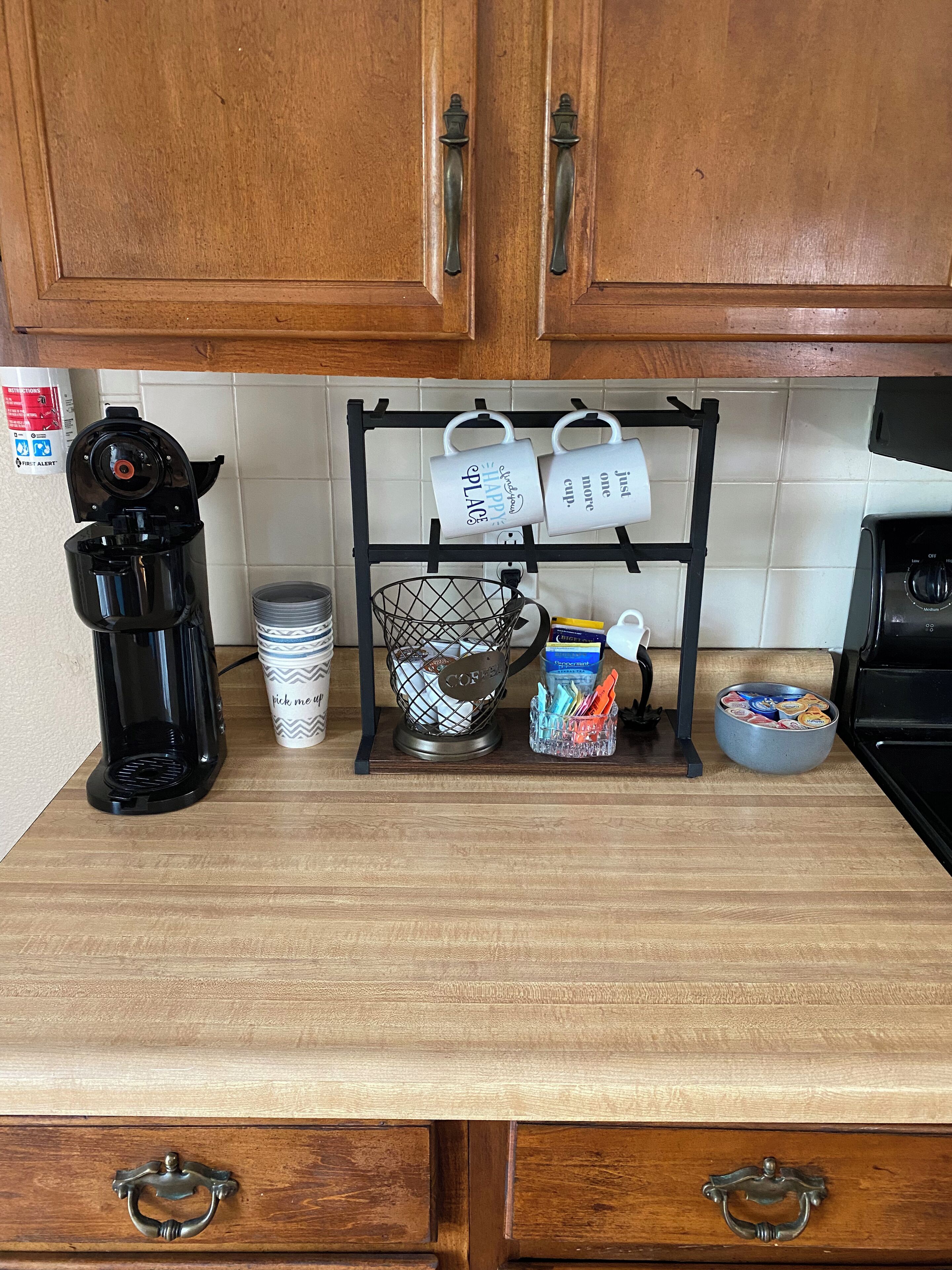 Un comptoir de cuisine avec une machine à café, des tasses, un panier et un bol rempli de collations.