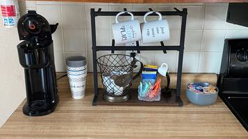 Un comptoir de cuisine avec une machine à café, des tasses, un panier et un bol rempli de collations.