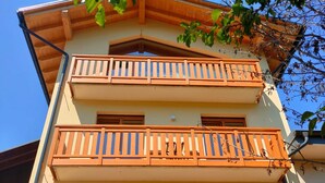 A multi-story building with balconies, a clear sky, and a tree in the foreground. - Room 1 - Nene Cristina with External Bathroom, Shared Terrace and Garden (Pieve di Cadore)