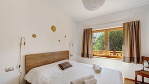 A bedroom with a wooden headboard, a bed with white linens, a window with curtains, and a view of greenery outside. - Room 1 - Nene Cristina with External Bathroom, Shared Terrace and Garden (Pieve di Cadore)