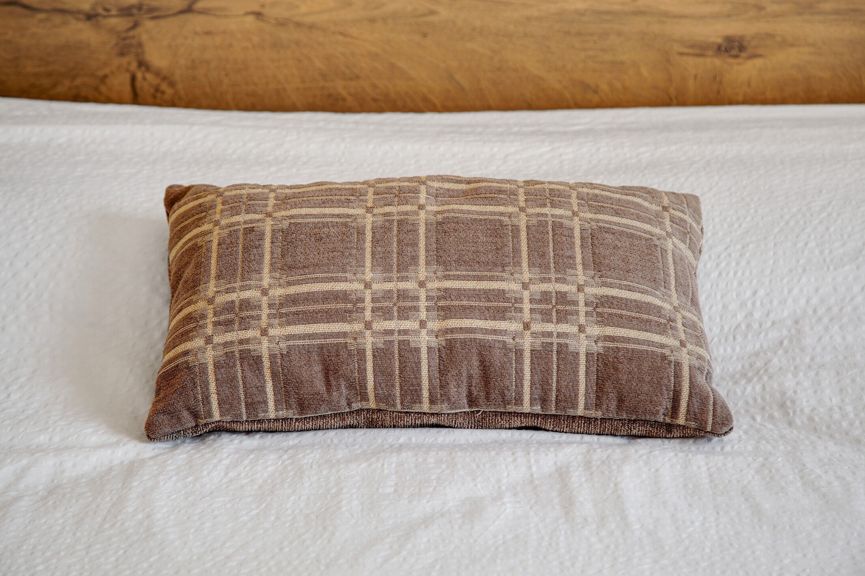 A pillow with a checkered pattern on a bed with white bedding.