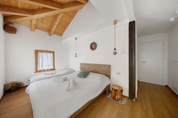 A bedroom with a wooden ceiling, a bed with white bedding, a window with curtains, and a wooden floor.