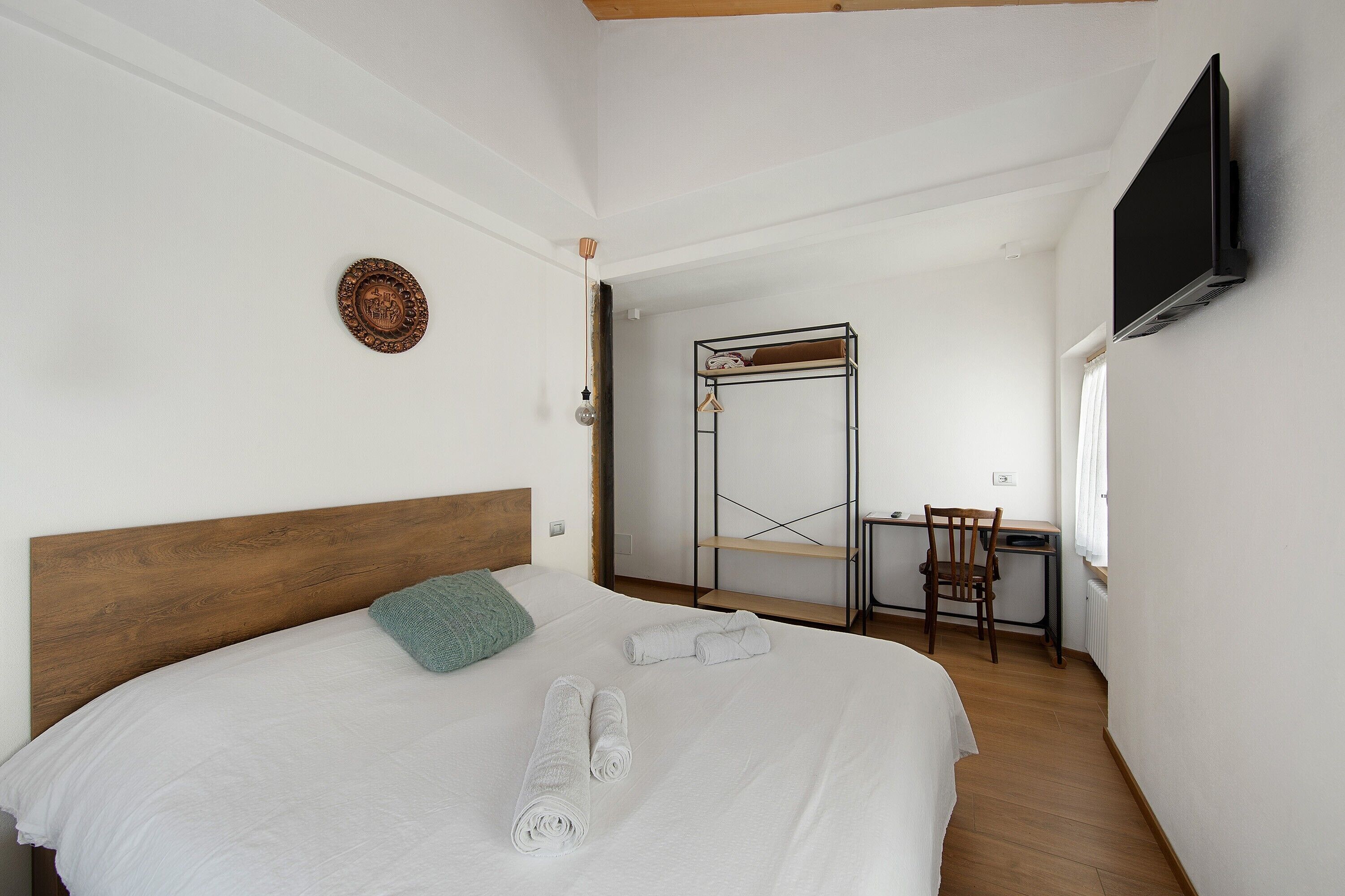 Ein Schlafzimmer mit einem Bett, einem Schreibtisch, einem Stuhl und einem an der Wand befestigten Fernseher.