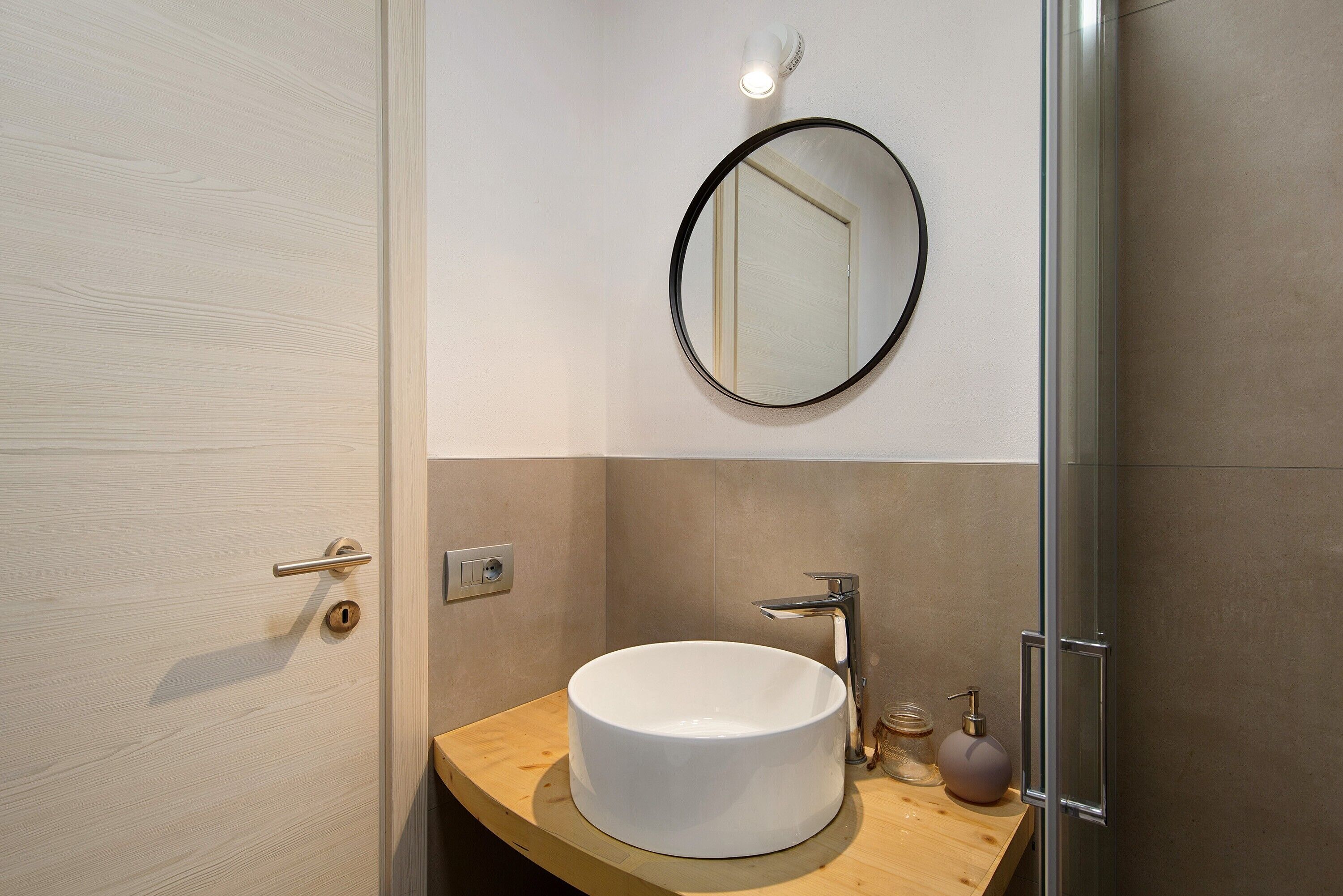A modern bathroom with a round mirror, a white sink, and a shower area.