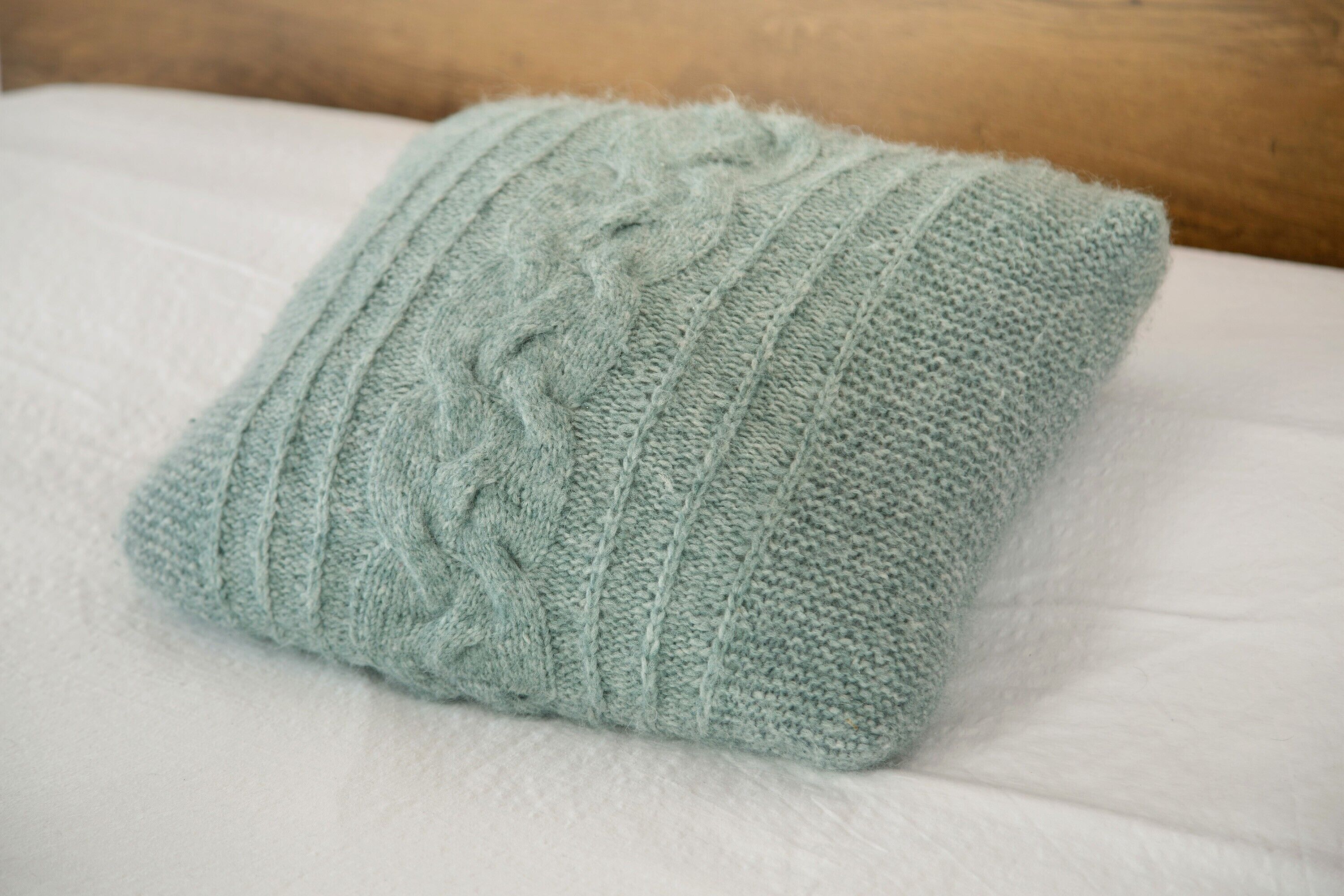 A light blue knitted pillow on a white bed.