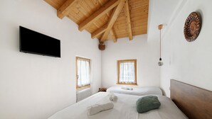 Un dormitorio con dos camas, un televisor de pantalla plana, vigas de techo de madera y una lámpara fijada a la pared.