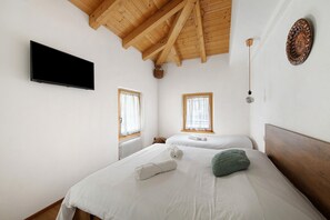 Una habitació amb dos llits, televisió de pantalla plana, bigues de sostre de fusta i una làmpada penjant a la paret.