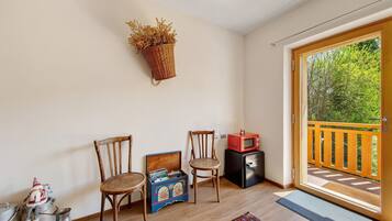Una habitación con dos sillas de madera, una cesta de mimbre en la pared, un electrodoméstico negro pequeño y una puerta de madera que da a un balcón.
