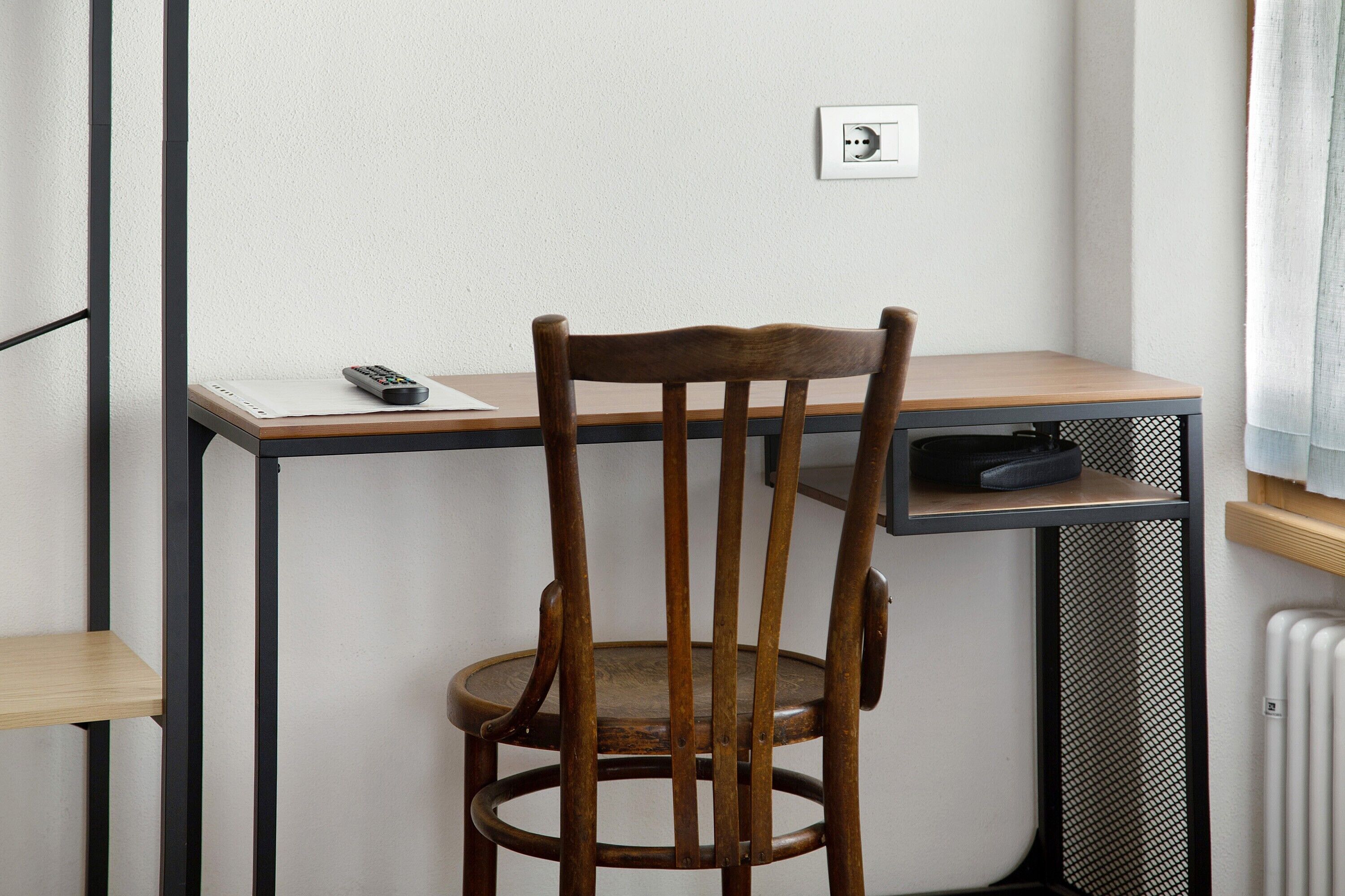 A wooden chair with a high backrest, a small table with a remote control, and a power outlet on the wall.