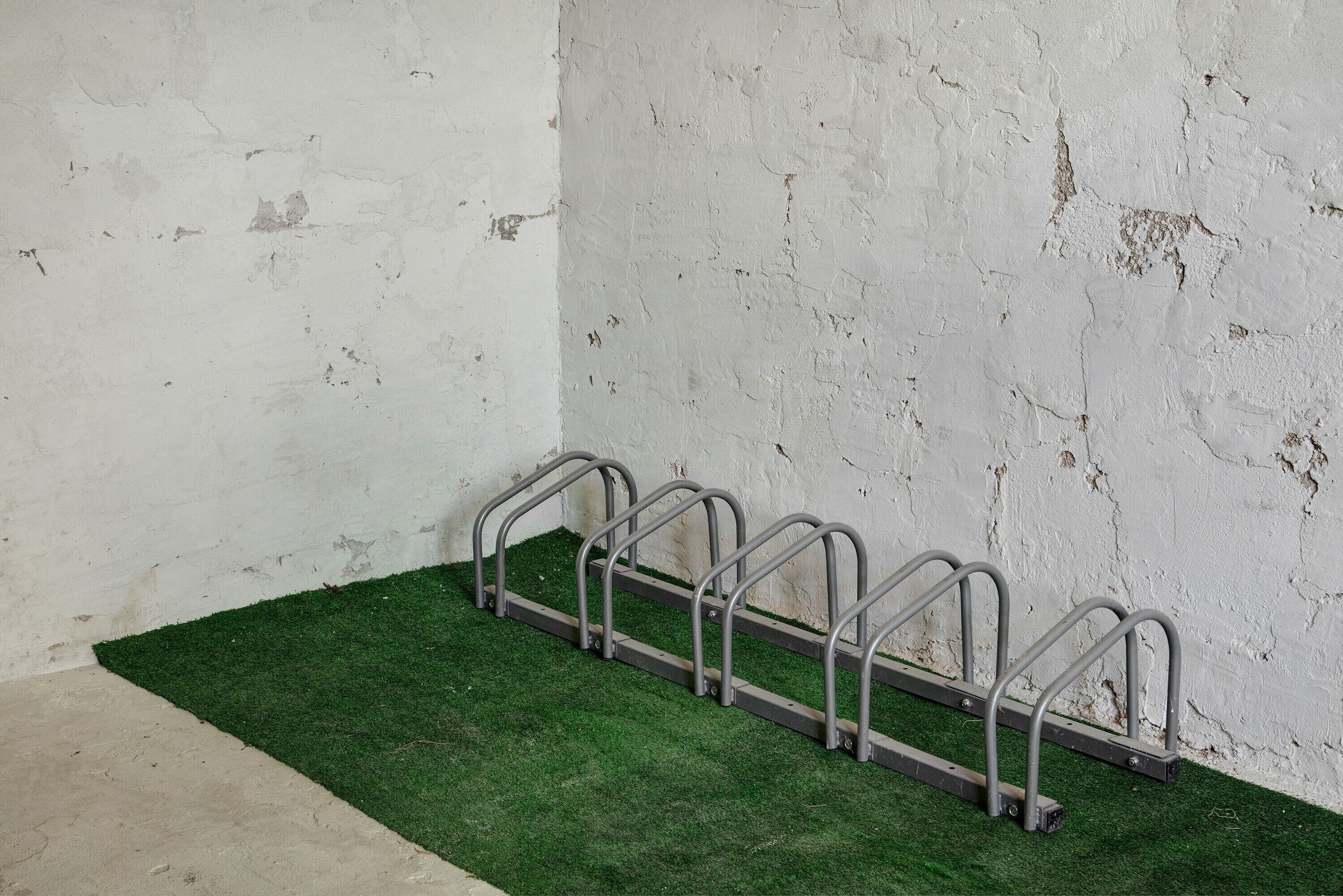 Diverses parades metàl·liques per bicicletes adossades a una paret blanca, amb un sòl de gespa artificial verda.