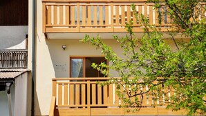 Un edificio de dos pisos con balcones de madera, una puerta visible y una ventana.