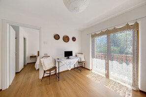 A room with a wooden floor, a table with a TV, two chairs, a window with lace curtains, and a balcony. - Room 4 – Nene Maria with Terrace and Shared Garden (Pieve di Cadore)