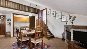 Un coin repas avec une table et des chaises en bois, un escalier, une cheminée et des tableaux encadrés au mur.