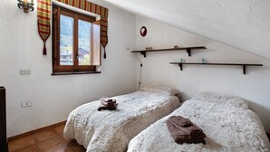 Une chambre avec deux lits, une fenêtre avec des rideaux, une étagère fixée au mur et une prise de courant.