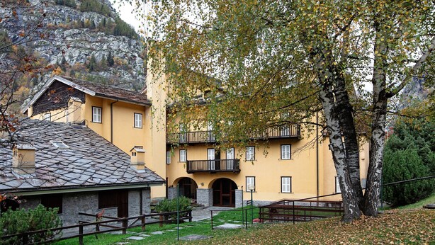 Un bâtiment jaune avec un toit en pierre, un balcon et un arbre devant.