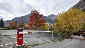 Un parking sécurisé, délimité par une barrière rouge et blanche, agrémenté d’un panneau d’avertissement et offrant un paysage montagneux en arrière-plan.