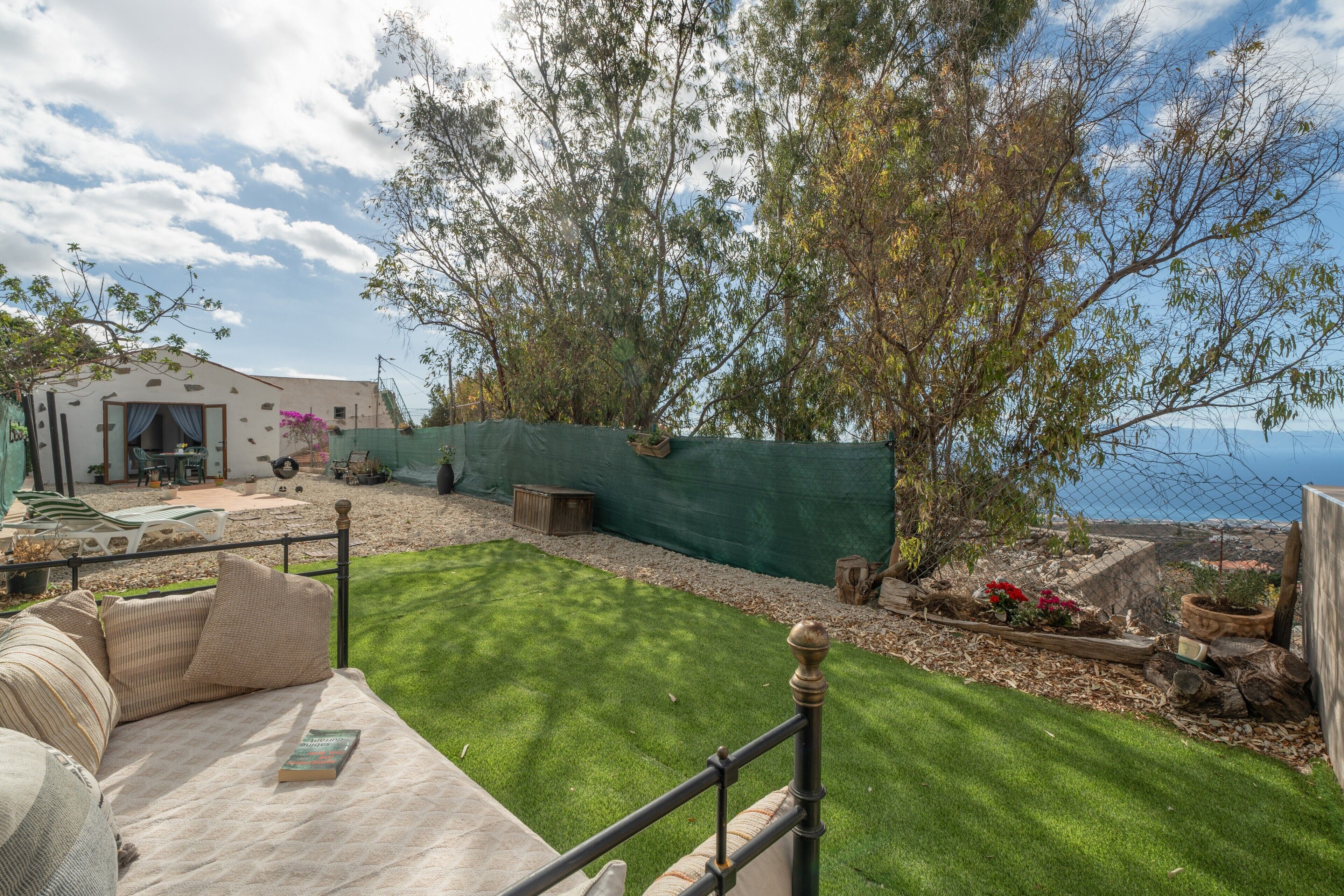 Un patio con césped, una zona de estar cubierta y vista al mar.