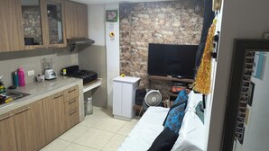 A compact kitchen with wooden cabinets, a built-in stove, and a small refrigerator. A flat-screen TV is mounted on the wall, and a fan is on the floor. - Cozy studio with WiFi and AC in charming Cartagena (Cartagena)